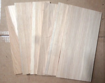 May include: A collection of five rectangular, light-colored wood veneer sheets. The sheets are arranged in a slightly fanned-out pattern, showcasing the natural grain and texture of the wood. The wood appears to be unfinished, with a smooth surface and subtle variations in tone.