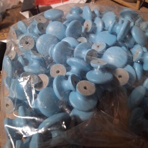 May include: A large bag filled with light blue plastic cabinet knobs. The knobs have a round shape with a raised center.