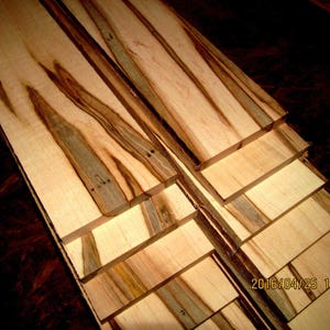 May include: Stack of six wooden boards with a unique wood grain pattern. The boards are light brown with dark brown streaks. The boards are stacked on top of each other, with the top board being the largest.