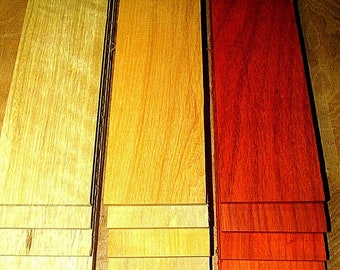 May include: Three stacks of wooden planks in varying shades of color. The planks range from light yellow to a vibrant red-orange hue. The wood grain is visible, and the planks are arranged vertically.