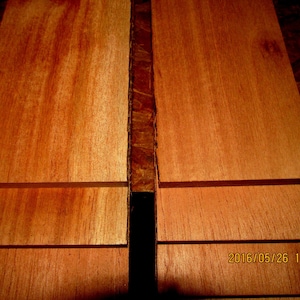 May include: Stacked wooden boards with a reddish-brown color and a smooth, polished surface. The boards are arranged in a vertical orientation, with the grain running horizontally.