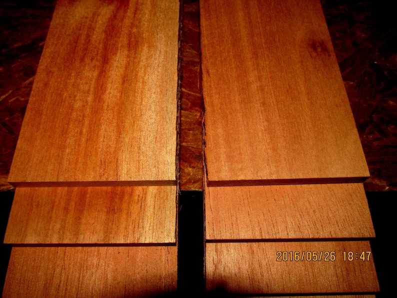 May include: Stacked wooden boards with a reddish-brown color and a smooth, polished surface. The boards are arranged in a vertical orientation, with the grain running horizontally.