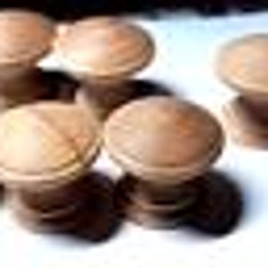 May include: Five wooden knobs with a smooth, rounded top and a cylindrical base. The knobs are a light brown color and have a natural wood finish.