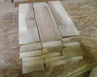 May include: A collection of unfinished wooden planks, varying in size, stacked and arranged on a light-colored surface. The wood has a natural, light brown color with visible grain patterns, suggesting it is ready for woodworking projects.