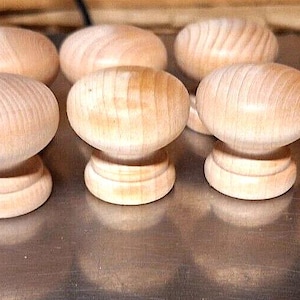 May include: A collection of ten unfinished wooden knobs, each with a rounded top and a cylindrical base. The knobs are arranged in a row on a silver surface.