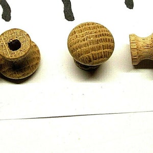 May include: Four wooden knobs in various styles. Two knobs are round with a small hole in the center. One knob is round with a raised pattern. One knob is cylindrical with a rounded top.