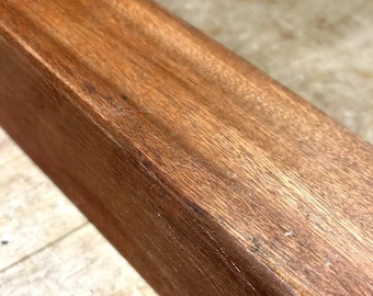 Könnte beinhalten: Nahaufnahme eines rechteckigen Holzstücks mit einer glatten, braunen Oberfläche. Das Holz hat eine natürliche Maserung und scheint mit einer klaren Beschichtung versehen zu sein.