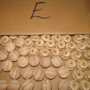 May include: A box filled with a large quantity of wooden knobs. The knobs are round and have a natural wood finish. The box is labeled with the letter "E".