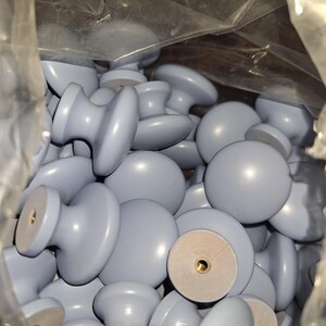 May include: A bag filled with a large quantity of light blue cabinet knobs. The knobs are round with a small, raised center.