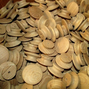 May include: A collection of unfinished wooden spools and knobs. The spools have a cylindrical shape with a central hole, while the knobs are round. The wood grain is visible, and the pieces are a light brown color. These components are likely for crafts or woodworking projects.