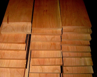 May include: Stacks of unfinished, light brown wooden planks. The planks are arranged in three stacks, with each plank showing the natural wood grain. A metal ruler is visible at the bottom, providing scale.