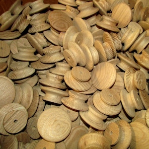 May include: A large pile of wooden knobs in various shades of brown. The knobs are round and have a raised center. They are all made of the same type of wood and have a similar grain pattern.