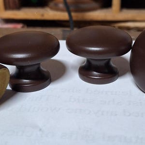May include: Four brown wooden cabinet knobs with a brass screw. The knobs are round and have a smooth finish.