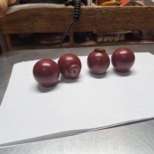 May include: Four dark brown wooden knobs with a brass screw in the center. The knobs are arranged in a row on a white surface.
