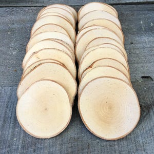 May include: A stack of 20 natural wood slices, each with a smooth, light brown surface and a visible grain pattern. The wood slices are arranged in two rows of ten, with the top of each slice facing the viewer.