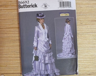 May include: A vintage sewing pattern for a dress with a long train. The pattern is for sizes 6-8-10-12-14 and is from Butterick. The pattern is called "History" and features a woman wearing a lavender dress with a white lace bodice and a matching hat.
