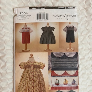 May include: A sewing pattern package featuring children's clothing designs. The package includes images of dresses and rompers in various styles, with details like smocking and sailboat embroidery. The package has the text "7504" and "Teresa Layman Designs".