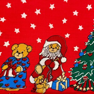May include: A festive red fabric featuring white stars and cartoon teddy bears dressed for Christmas. One bear is dressed as Santa Claus, and another is wearing blue pajamas with red hearts. A decorated Christmas tree is also present.