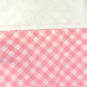 May include: A close-up of a white fabric and a pink and white gingham pattern. The white fabric is at the top, and the gingham pattern is below. The gingham pattern is a classic design, with evenly spaced squares.