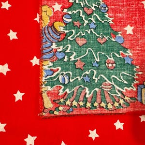 May include: A festive Christmas-themed fabric with a red background and white stars. The fabric features a green Christmas tree decorated with ornaments and a cartoon bear wearing a blue and white striped shirt.