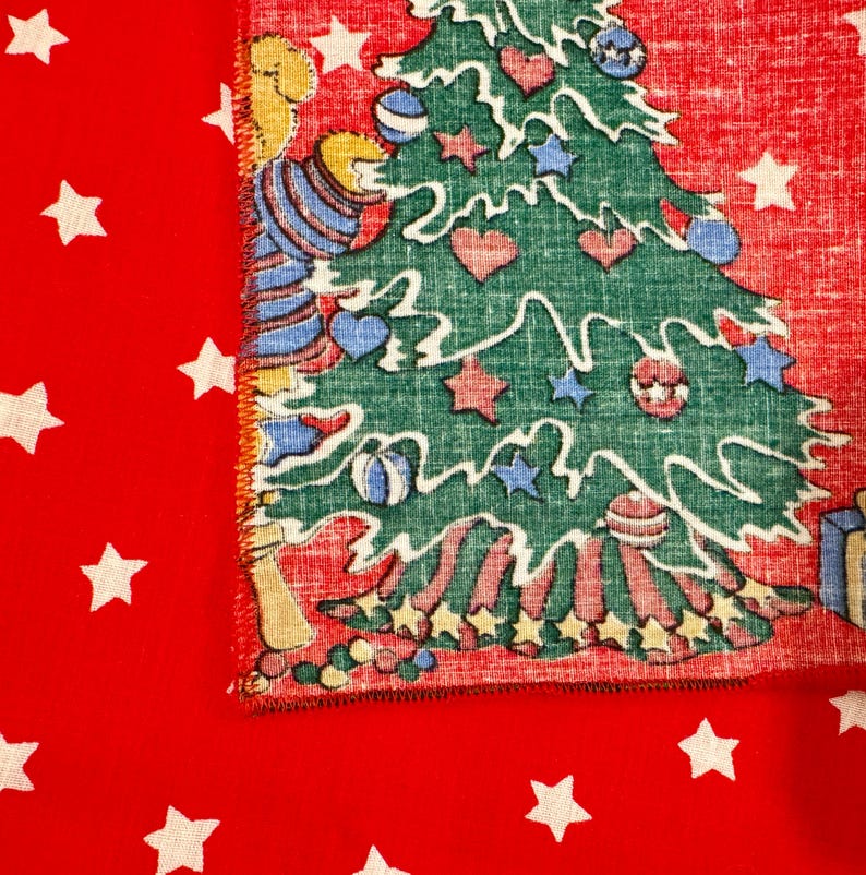 May include: A festive Christmas-themed fabric with a red background and white stars. The fabric features a green Christmas tree decorated with ornaments and a cartoon bear wearing a blue and white striped shirt.
