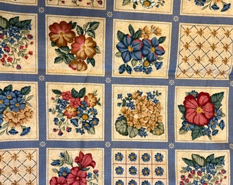 May include: Fabric with a repeating pattern of floral squares. Each square contains a different floral arrangement in red, blue, yellow, and white, set against a beige background. The squares are outlined with a light blue border.
