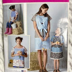 May include: Simplicity sewing pattern 8087 featuring apron and dress designs. The pattern includes multiple views with different fabric combinations, including floral and polka dot patterns. The size range is U.S. 3-8/XS-XL.