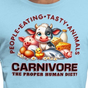 May include: A light blue t-shirt with a cartoon illustration of a cow, pig, fish, chicken, and eggs. The text "People Eating Tasty Animals Carnivore The Proper Human Diet!" is printed in red and black.
