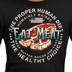 May include: A black t-shirt with a white circle graphic that says "The Proper Human Diet... Eat Meat... The Healthy Choice" with a red and white steak graphic in the centre. The graphic also includes the text "Humanly Raised U.S. Grown Beef Butter Bacon and Eggs."