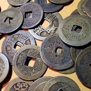 Puede incluir: Una colecci&oacute;n de monedas chinas antiguas con un agujero cuadrado en el centro. Las monedas son de bronce y tienen caracteres chinos inscritos en ellas.