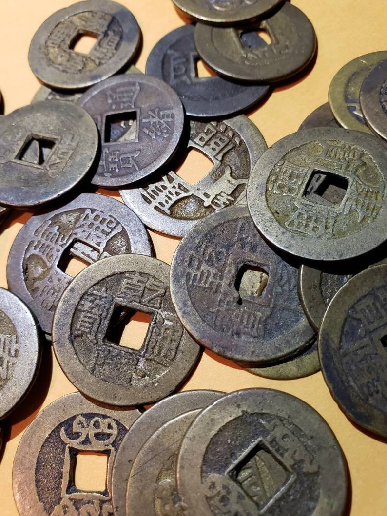 Puede incluir: Una colecci&oacute;n de monedas chinas antiguas con un agujero cuadrado en el centro. Las monedas son de bronce y tienen caracteres chinos inscritos en ellas.