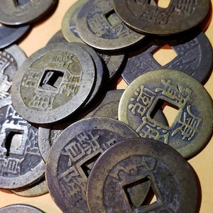 Puede incluir: Una colecci&oacute;n de monedas chinas antiguas con un agujero cuadrado en el centro. Las monedas est&aacute;n hechas de bronce y tienen dise&ntilde;os y caracteres intrincados.