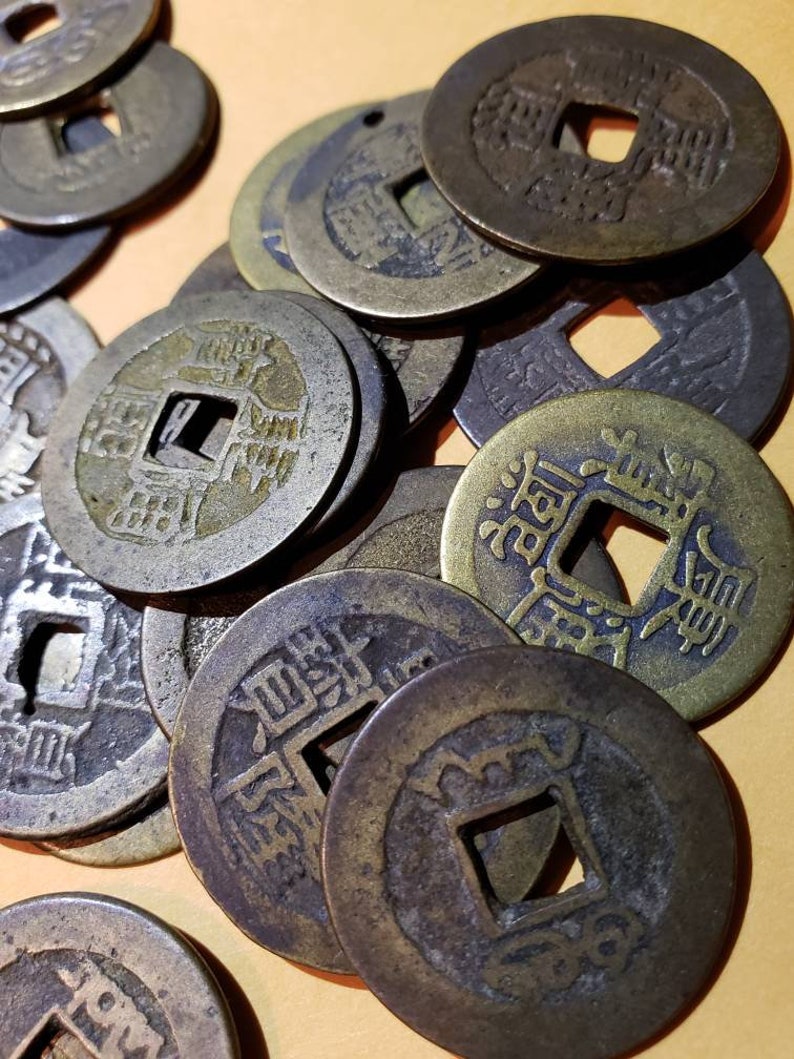 Puede incluir: Una colecci&oacute;n de monedas chinas antiguas con un agujero cuadrado en el centro. Las monedas est&aacute;n hechas de bronce y tienen dise&ntilde;os y caracteres intrincados.