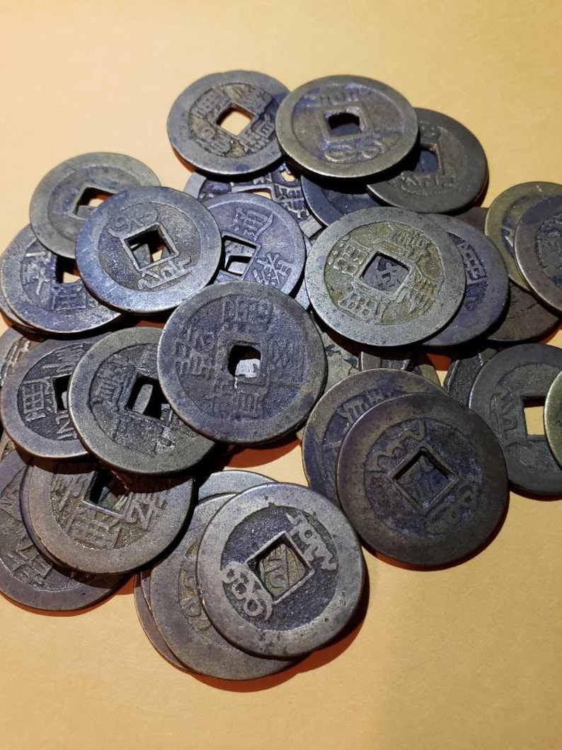 Puede incluir: Un mont&oacute;n de monedas chinas antiguas con agujeros cuadrados en el centro. Las monedas son de bronce y tienen caracteres chinos.