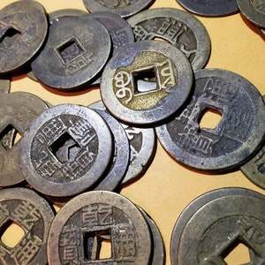 Puede incluir: Una colecci&oacute;n de monedas chinas antiguas con un agujero cuadrado en el centro. Las monedas est&aacute;n hechas de bronce y tienen caracteres chinos inscritos en ellas.