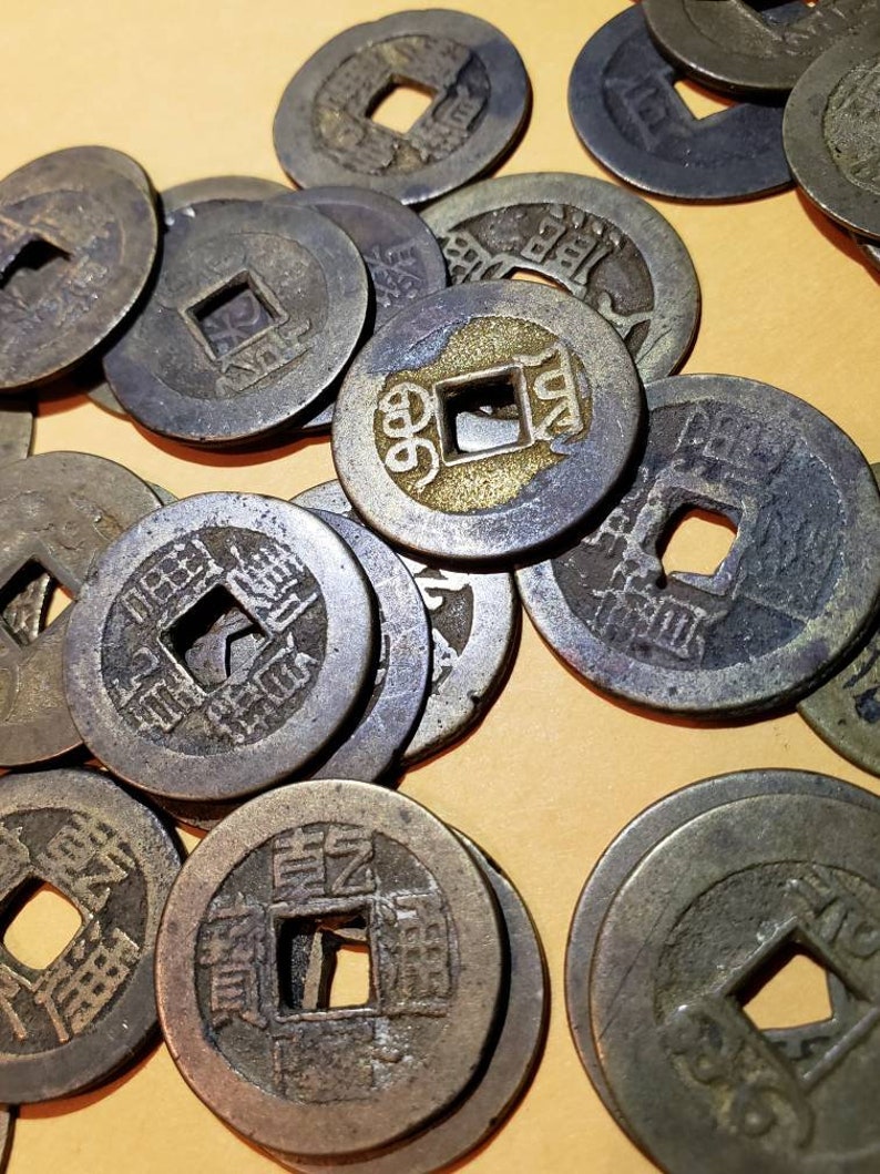 Puede incluir: Una colecci&oacute;n de monedas chinas antiguas con un agujero cuadrado en el centro. Las monedas est&aacute;n hechas de bronce y tienen caracteres chinos inscritos en ellas.