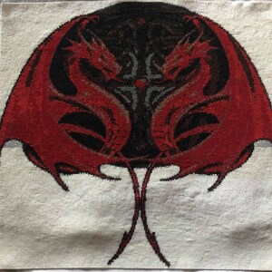 May include: Cross-stitch design featuring two red dragons with outstretched wings, facing each other against a black background. The dragons are detailed with black accents, and the design is set on a white fabric.
