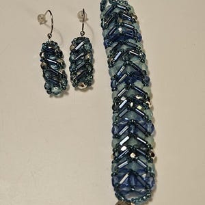 May include: A beaded jewelry set featuring a bracelet and matching earrings. The bracelet and earrings are primarily blue with silver accents. The bracelet has a decorative clasp. The earrings are dangle style. The number "1335" is visible in the image.