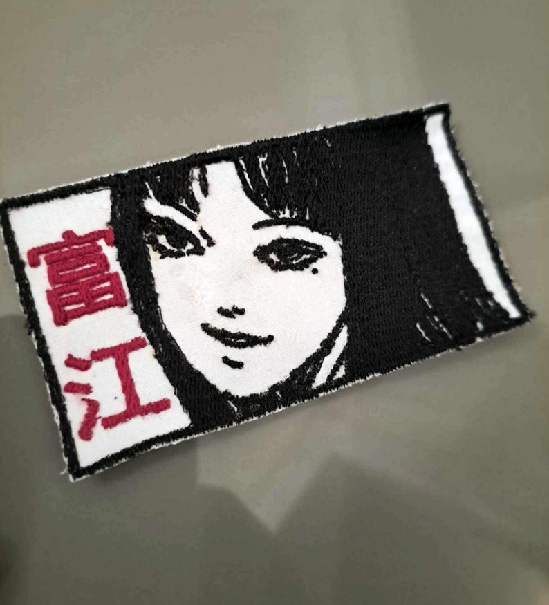 May include: White embroidered patch with a black and white image of a woman's face and the text "真紅" in red.