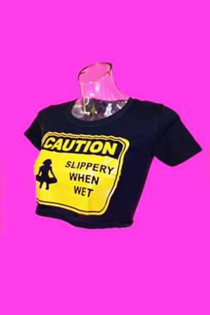 May include: Black cropped t-shirt with a yellow caution sign that says "CAUTION SLIPPERY WHEN WET".