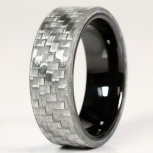 May include: A ring with a woven grey carbon fibre exterior and a glossy black interior. The ring has a smooth, rounded shape and a modern design. The carbon fibre pattern is clearly visible. The ring's width is approximately 0.8 cm.
