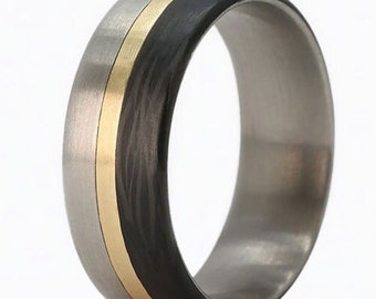 May include: A close-up of a ring with a brushed silver band, a central gold stripe, and a black carbon fiber inlay. The ring has a modern, minimalist design.
