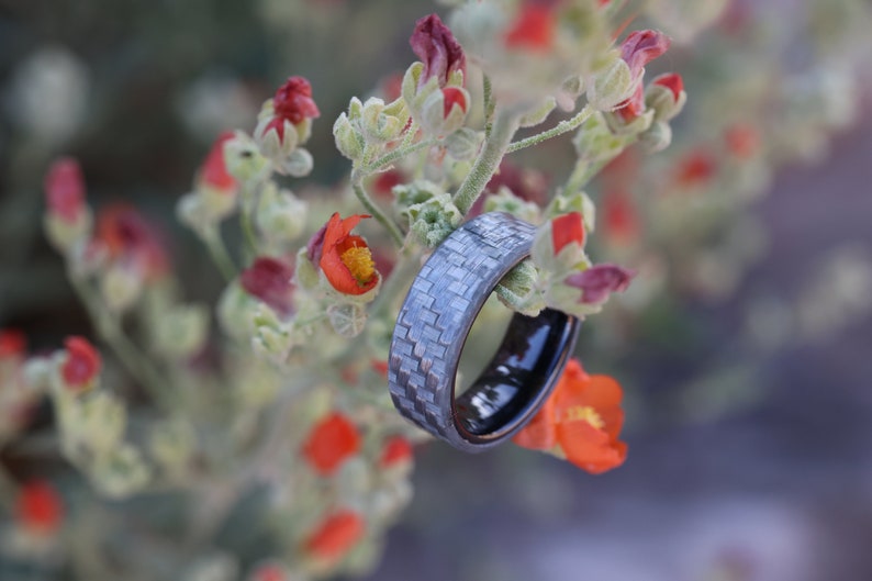May include: A silver ring with a textured design, set against a backdrop of orange and red flowers. The ring has a black interior. The image is a close-up, with the ring as the main focus.
