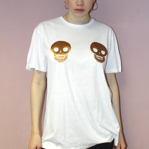 May include: White t-shirt with two gold skull designs on the front.