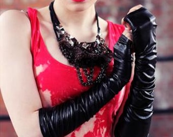 May include: A woman with short, spiky blonde hair wears a red tank top and black leather gloves. She is wearing a silver and black necklace.