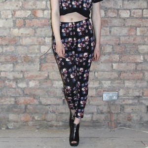 May include: A woman wearing a black and floral print crop top and matching pants. The top has a short sleeve and a fitted silhouette. The pants are a slim fit and have a floral print.