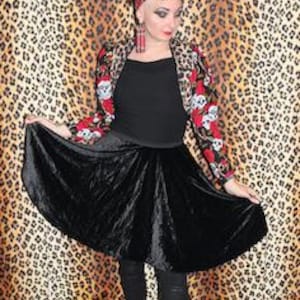 May include: A woman wearing a black velvet skirt with a red and black skull print jacket. She is wearing black boots and has a red and black bandana tied around her head.