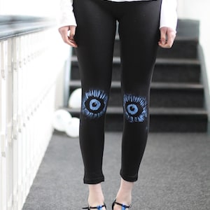 Könnte beinhalten: Schwarze Leggings mit blauen Augenmotiven auf den Knien. Die Person trägt blaue glitzernde Absätze.