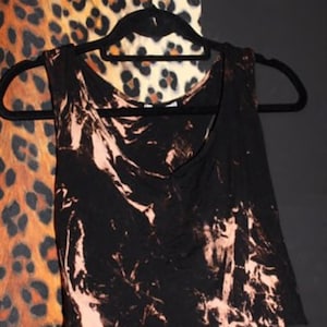 May include: A black tank top with a bleach-splattered design. The top has a scoop neck and a relaxed fit.