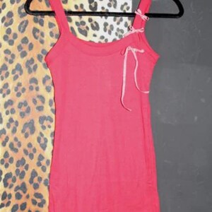 May include: A pink sleeveless tank top with a white and pink ribbon tied at the neckline.